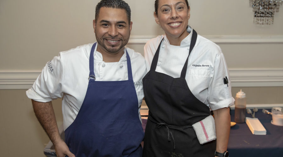 Two chefs in white uniforms and dark aprons smile for the camera, standing proudly side by side in a kitchen filled with cooking supplies. Their passion shines through as they support the Los Angeles Regional Food Bank, dedicated to nourishing their community.