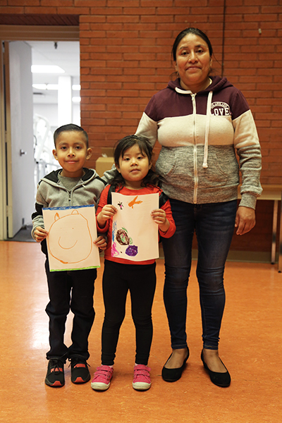 Mother and her two children, a smiling boy and girl, holding up their art work.