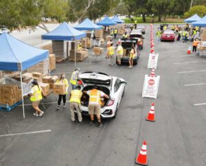 An aerial view of volunteers loading parked cars with food kits at a drive-through food distribution hosted by the LA Regional Food Bank.