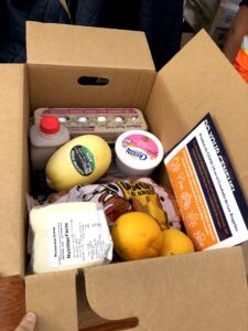 A food box containing chocolate milk, yogurt, eggs, cheese, fruit and potatoes.