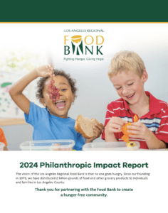 Two smiling children sit at a table enjoying snacks, with one holding up a piece of food. The image appears in the Los Angeles Regional Food Bank’s 2024 Philanthropic Impact Report, highlighting the impact behind their financials.