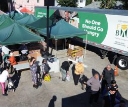 People wait in line at an outdoor WeFeedLA food distribution event next to a truck labeled 
