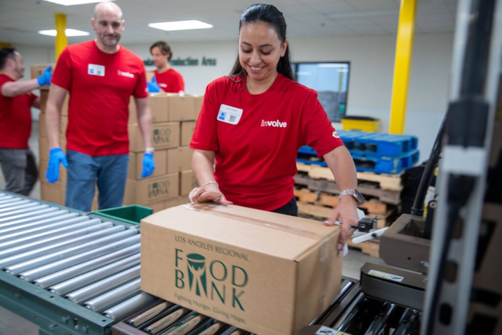 A woman in a red shirt smiles while placing a box labeled 