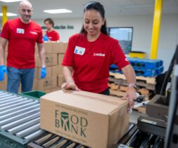 A woman in a red shirt smiles while placing a box labeled 