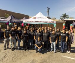 A group of people wearing matching black T-shirts pose and smile in front of tents labeled 