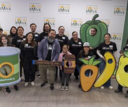 A group of people in UCLA Law shirts pose at a food bank under a banner that reads 