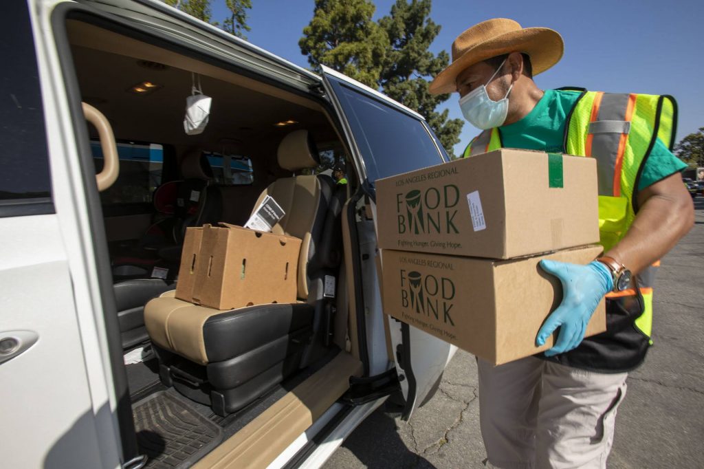 A Los Angeles Regional volunteer loads up a parked car with boxed food kits at a drive-through food distribution.