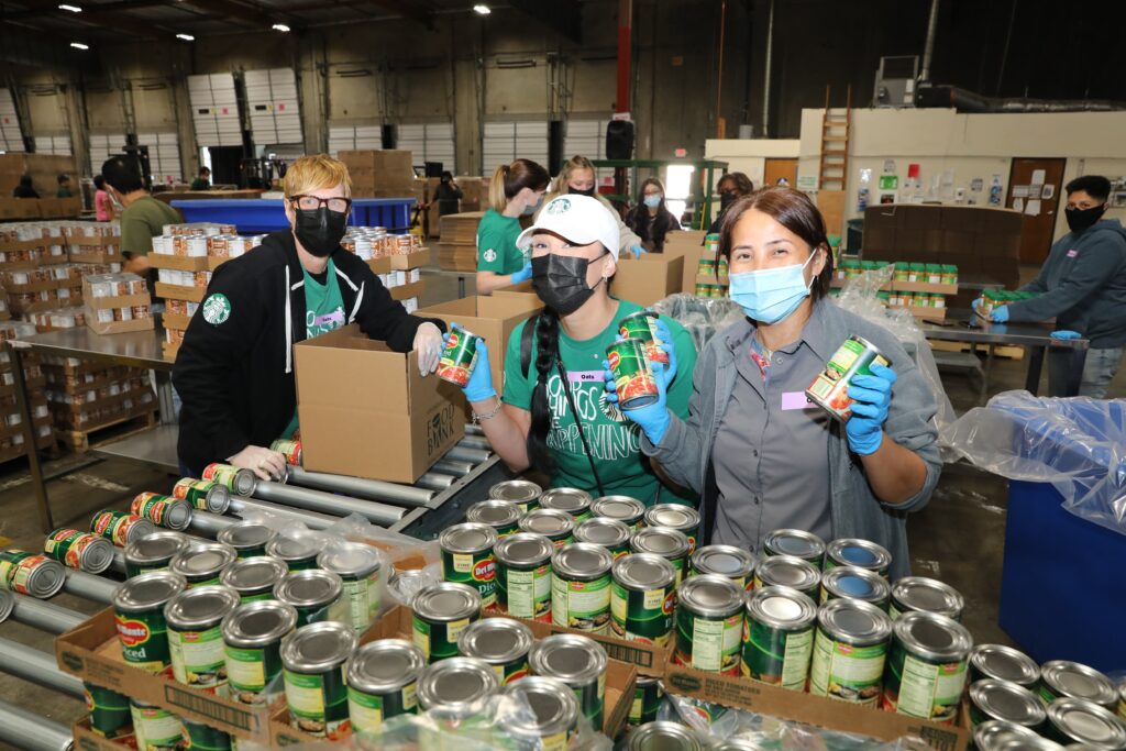 Three Starbucks employees hold up canned food items during a volunteer event at the LA Regional Food Bank