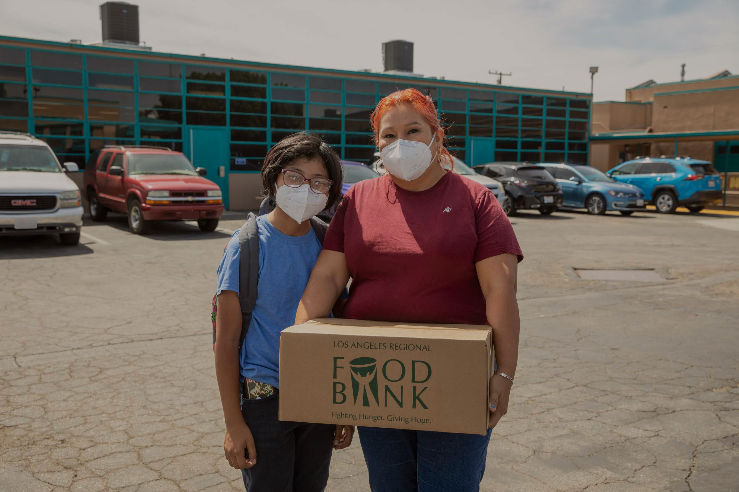 Patricia holding a Food Bank box, with her son, after a BackPack Program distribution at Mayo Elementary