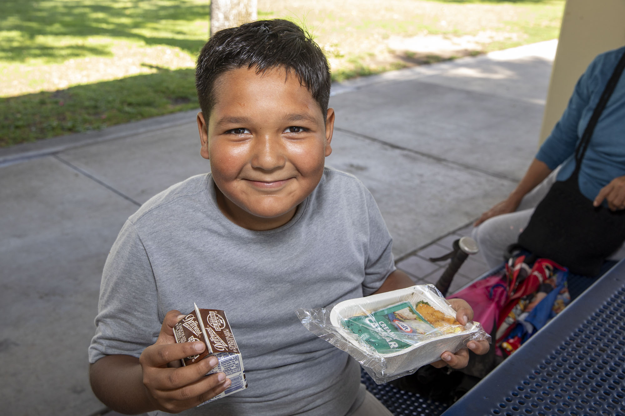 A small boy smiles with his lunch during a free summer meals distribution at Bristow Park during the 2023 summer