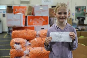 Maggie Williamson holds birthday check in front of carrots