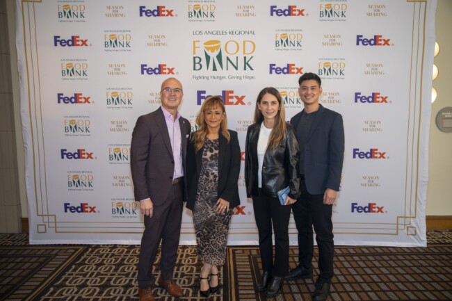 Four people stand smiling in front of a backdrop with logos for the Los Angeles Regional Food Bank and FedEx. They are dressed in formal attire on a patterned carpet.