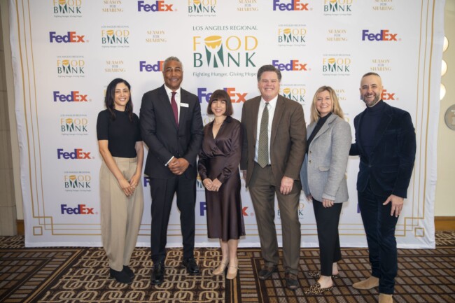 A group of six people standing in front of a backdrop with "Los Angeles Regional Food Bank" and "FedEx" logos. They are dressed in business attire and smiling at the camera.