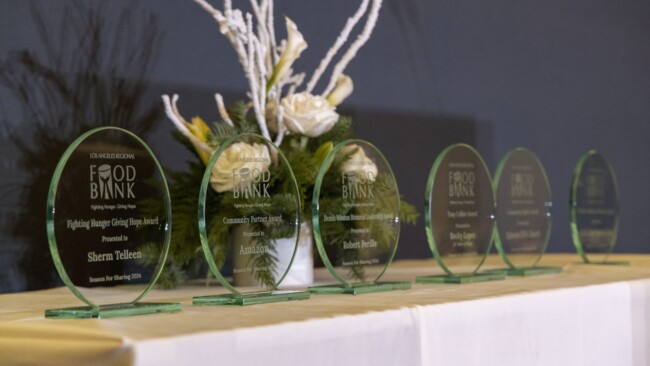 A row of green glass awards on a table, each inscribed with "Food Bank." White floral arrangement in the background, enhancing the elegant display.