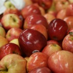 A close-up of a pile of apples, showcasing vibrant shades of red and yellow. Some apples bear stickers, reflecting their journey through the Los Angeles Regional Food Bank to nourish communities in need.