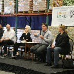 Five people sit on a stage engaging in a panel discussion. Behind them, shelves stacked with food boxes set the scene. A "Los Angeles Regional Food Bank" banner above, as part of the LA Times Food Bowl, reads "The Intersection of Hunger and Food Waste.
