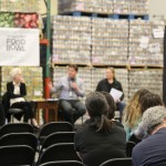 A panel discussion at the Los Angeles Regional Food Bank event features four speakers on stage. The backdrop showcases shelves of food boxes. Attendees are seated, listening intently as banners proclaim "Food Bank" and "Food Bowl.