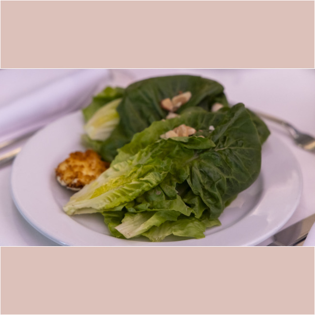 A white plate with a fresh green salad made of lettuce leaves, topped with almond slices, and accompanied by a small pastry on the side supports the efforts of the Los Angeles Regional Food Bank in promoting nutritious meals for everyone.
