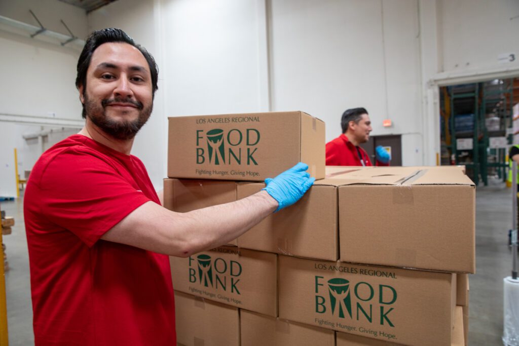 A man in a red shirt and blue gloves stands next to stacked boxes labeled 