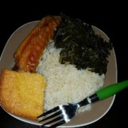 A plate of food from the Los Angeles Regional Food Bank featuring rice, collard greens, cornbread, and a piece of salmon, with a green-handled fork resting on the side.