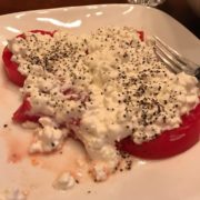 A plate with sliced tomatoes topped with creamy cottage cheese and sprinkled with black pepper, reminiscent of fresh produce often donated to the Los Angeles Regional Food Bank. A fork is placed on the side.