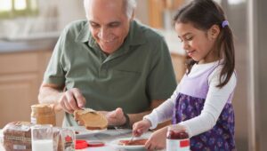 a grandfather making a peanut butter & jelly sandwich with his granddaughter