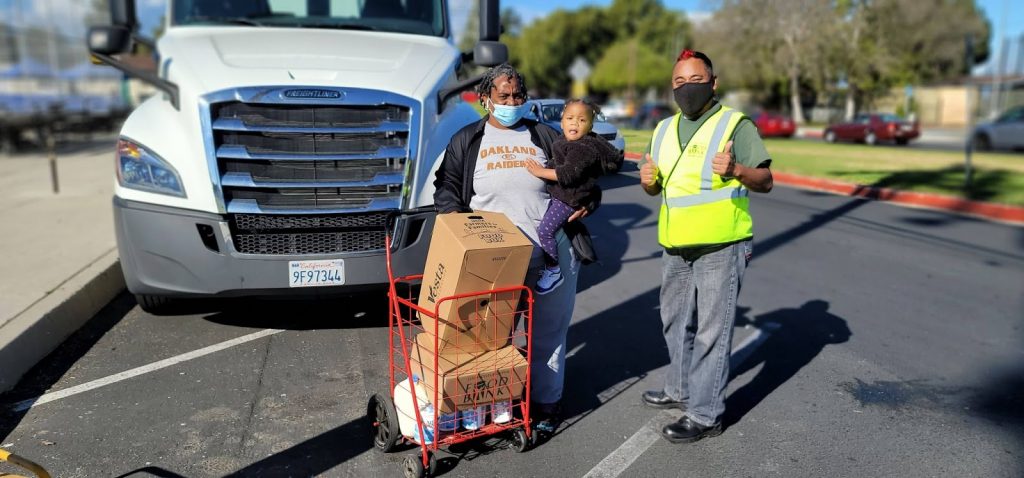 A LA Regional Food Bank employee helps a food recipient and her granddaughter with food boxes at a distribution.